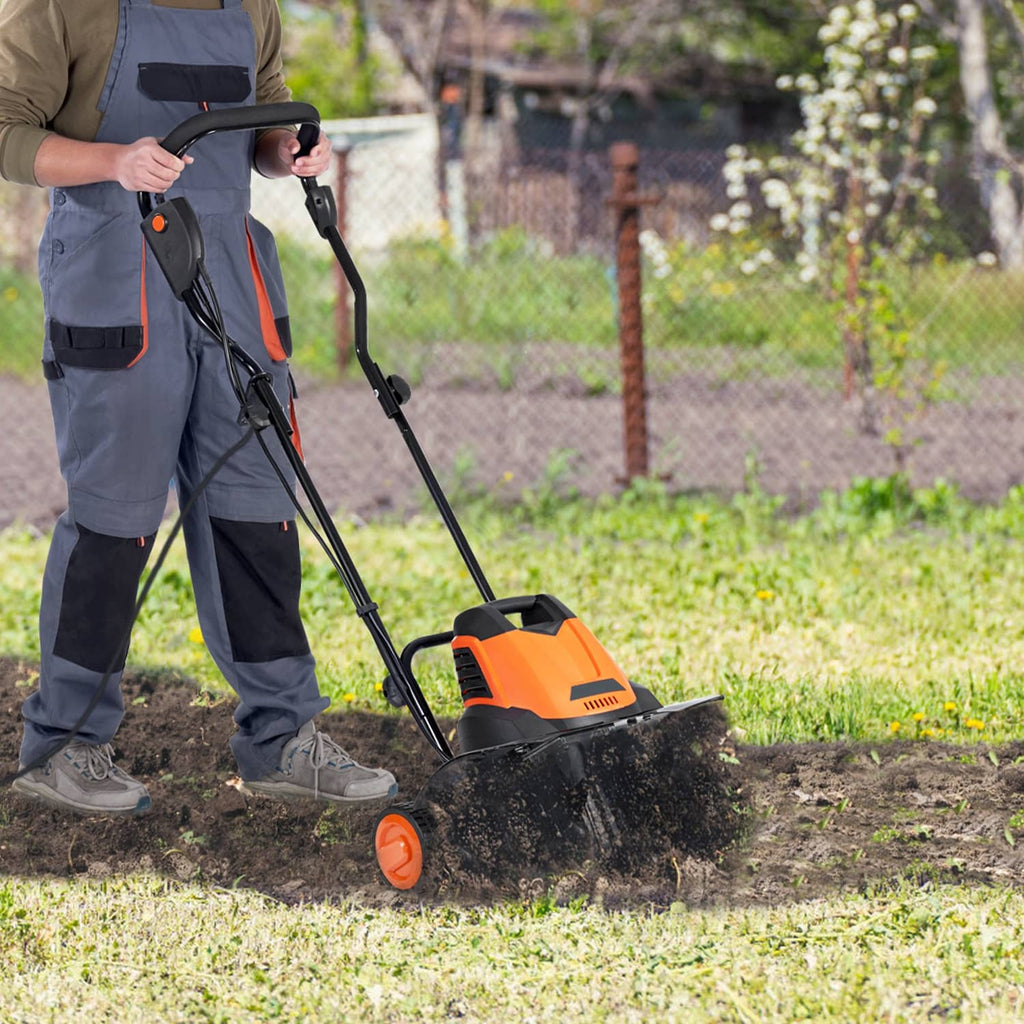 Electric garden tiller in use on grass and soil, with orange motor housing and tines