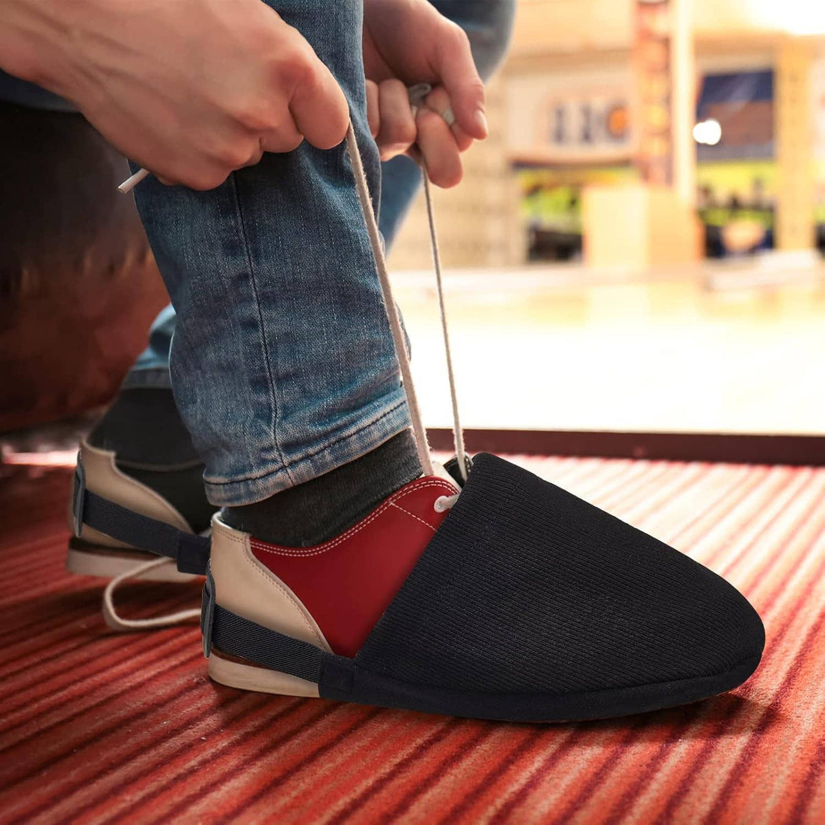 Black bowling shoe slider sock cover with elastic strap on a red-and-white sneaker