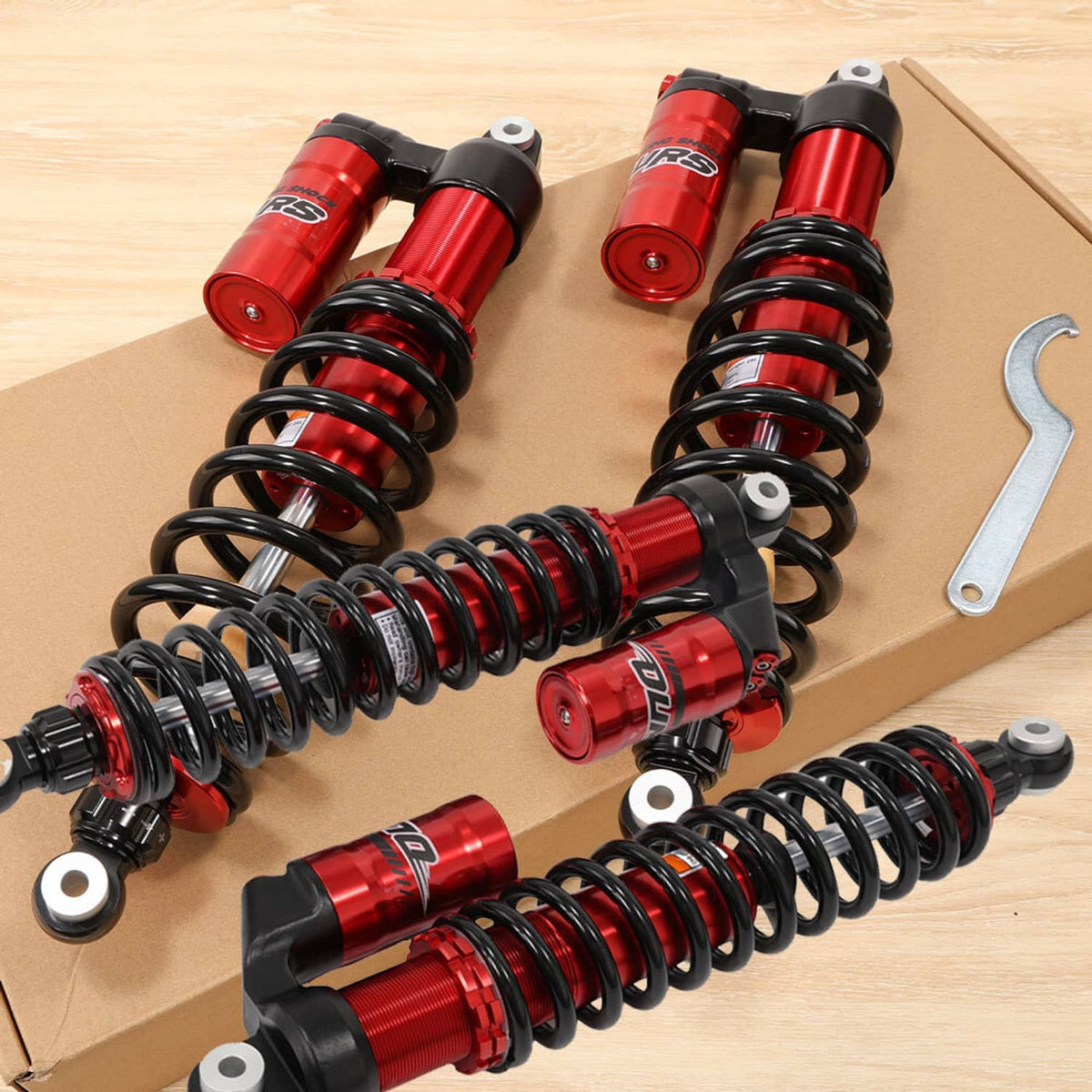 Two red shock absorbers with black coil springs on a cardboard backing, metal hook included
