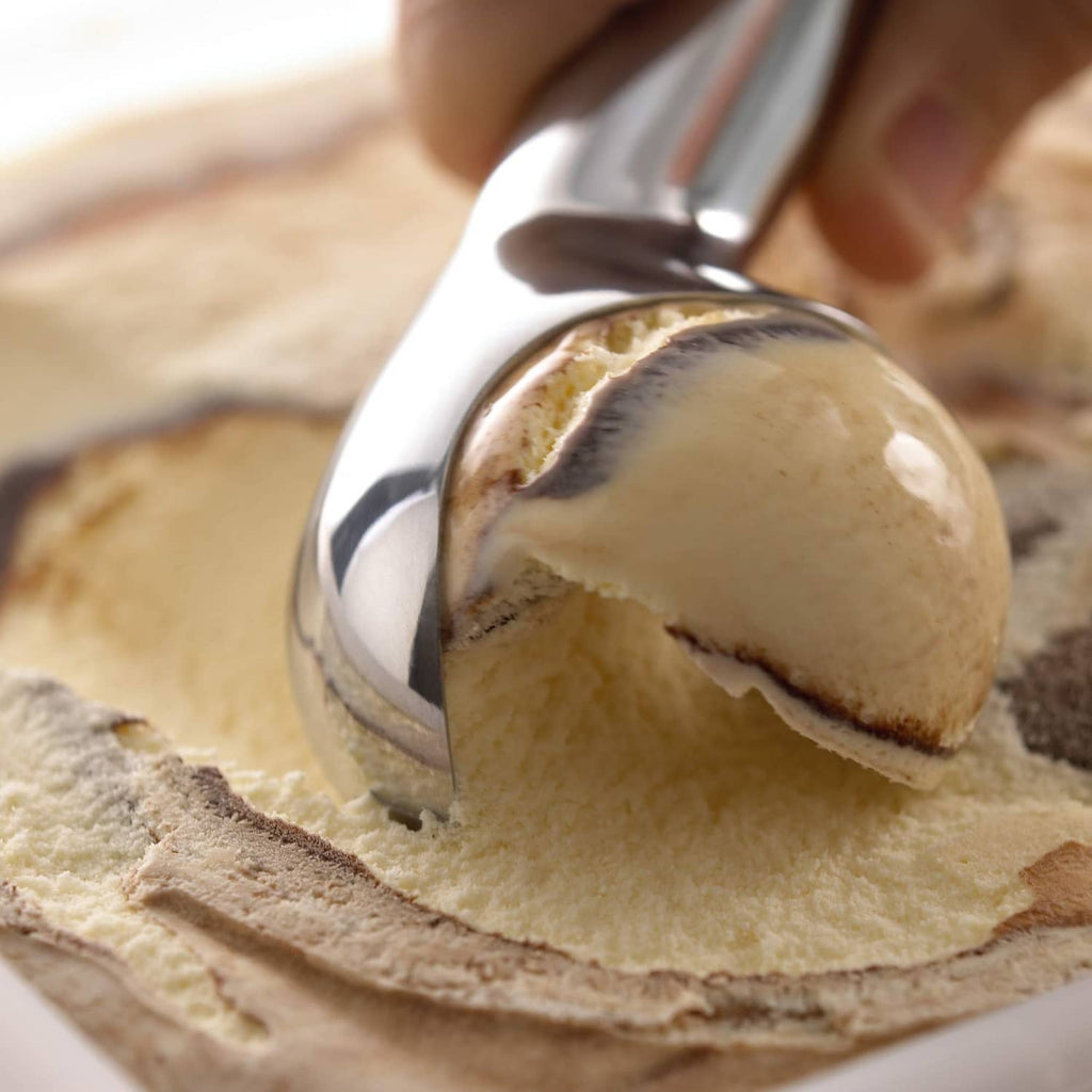 Stainless Zeroll scoop resting over a mound of ice cream on a flat surface.