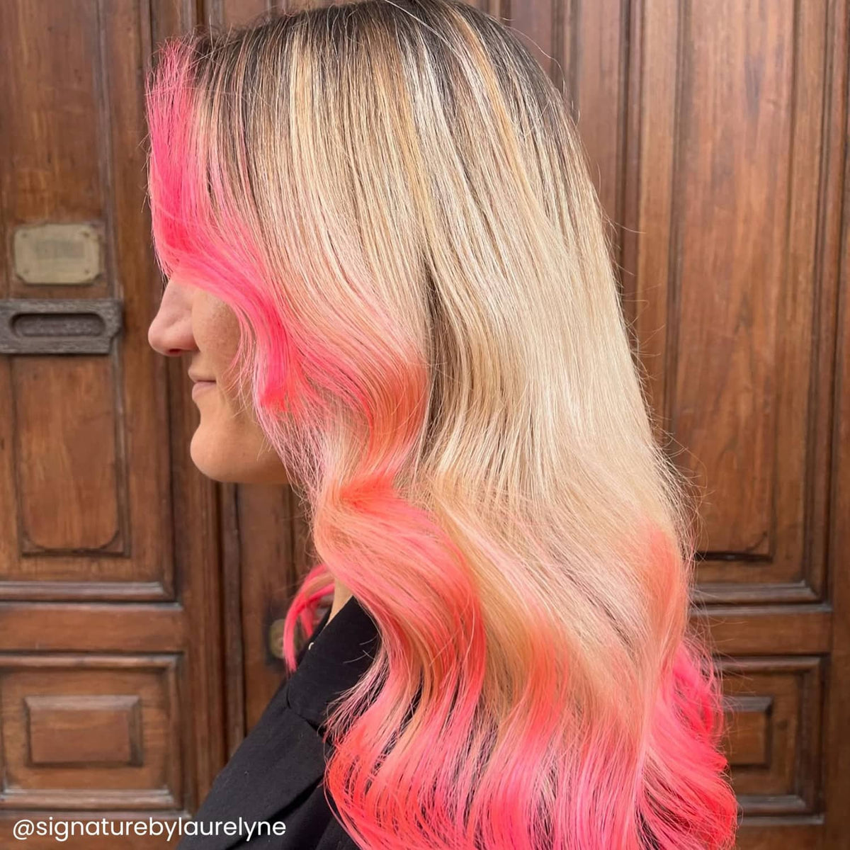 Long layered blonde hair with vivid coral-pink sections, side view