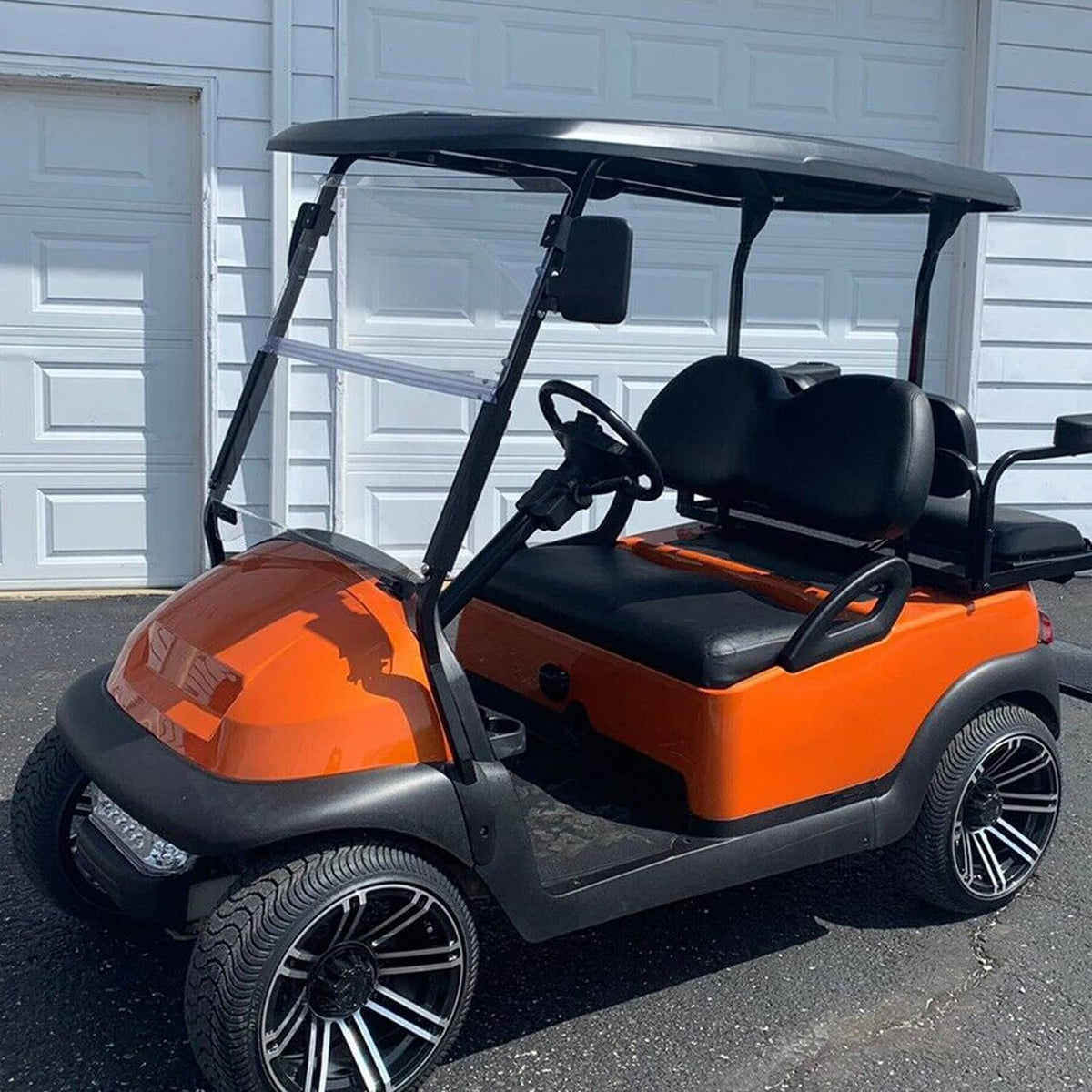 Clear windshield panel with black support frame on an orange golf cart.