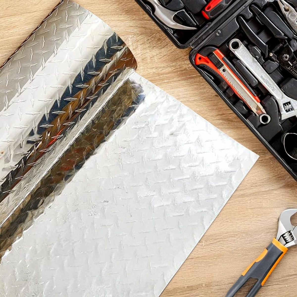 Rolled silver diamond plate aluminum sheet on wood with tools nearby