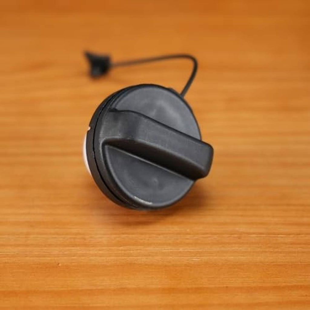 Gas cap with tether cord, black cover and ring base on a wooden surface.
