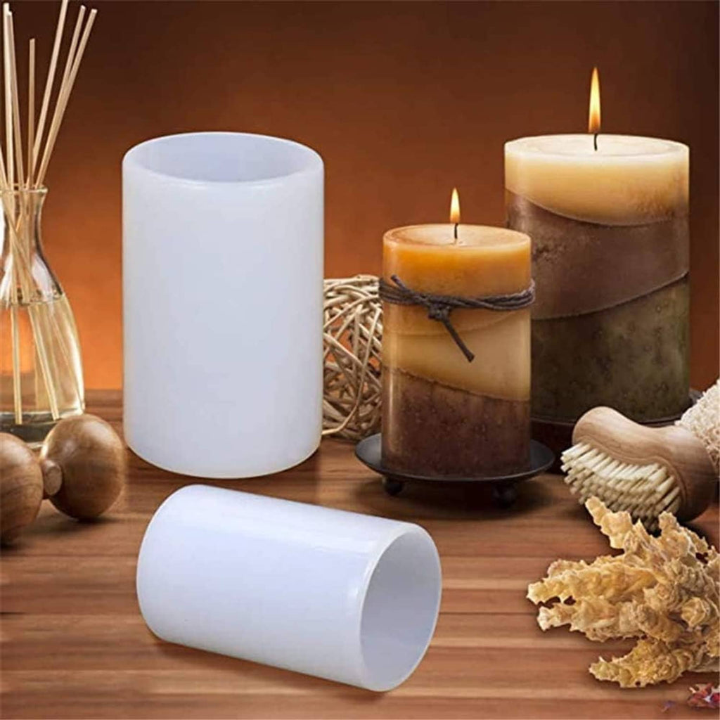 White cylinder candle molds on wooden table, with two pillar candles and supplies nearby.