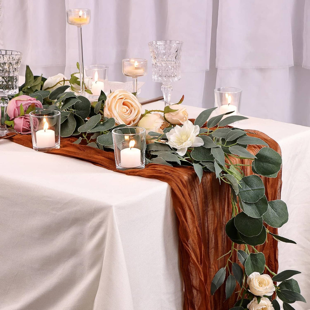 Clear glass votive candle holders with lit tea lights along a table runner
