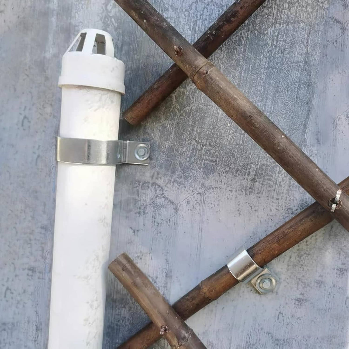 One-hole pipe clamp holding a white pipe to a metal-and-wood pipe rack