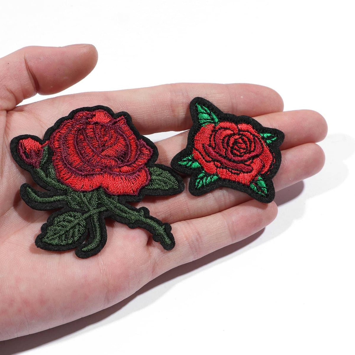 Two embroidered red rose patches with green leaves, shown on a hand