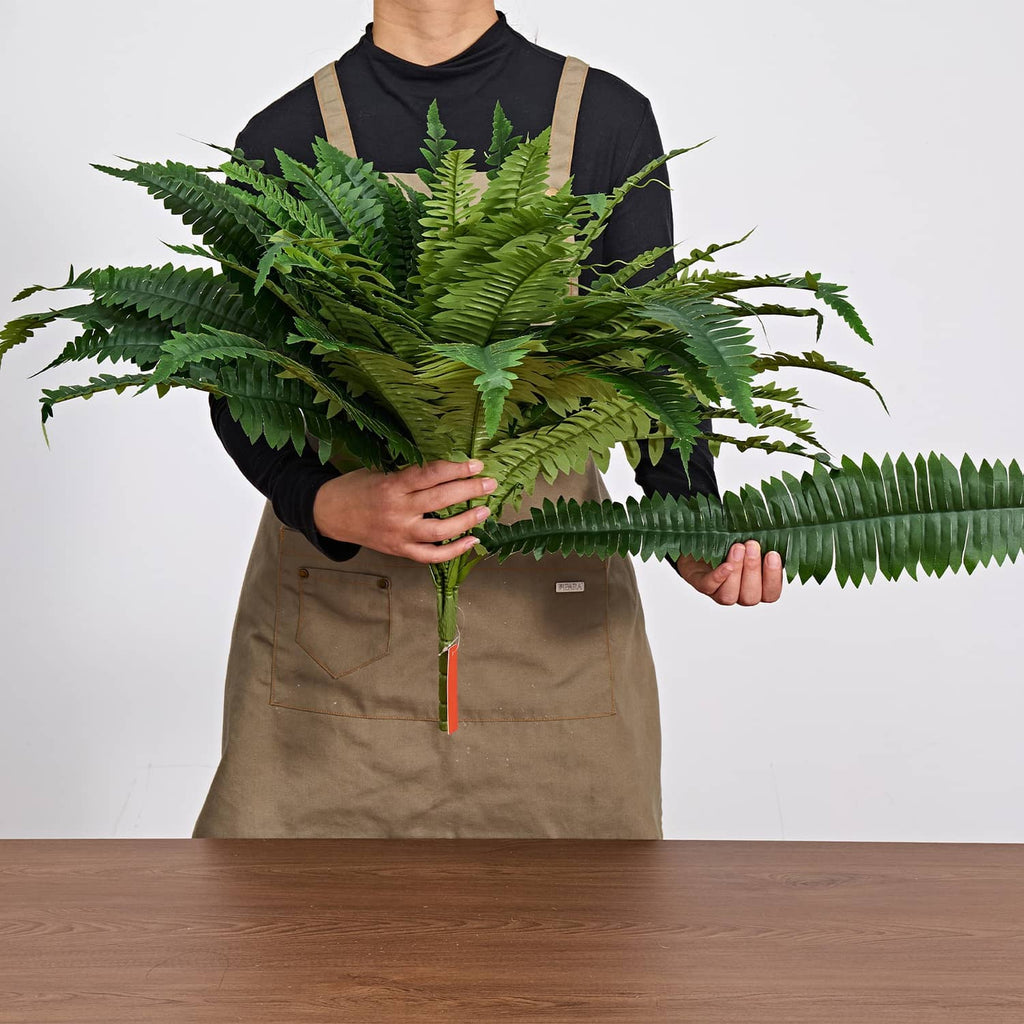 Artificial green fern plant held with full frond spread, flexible artificial leaves