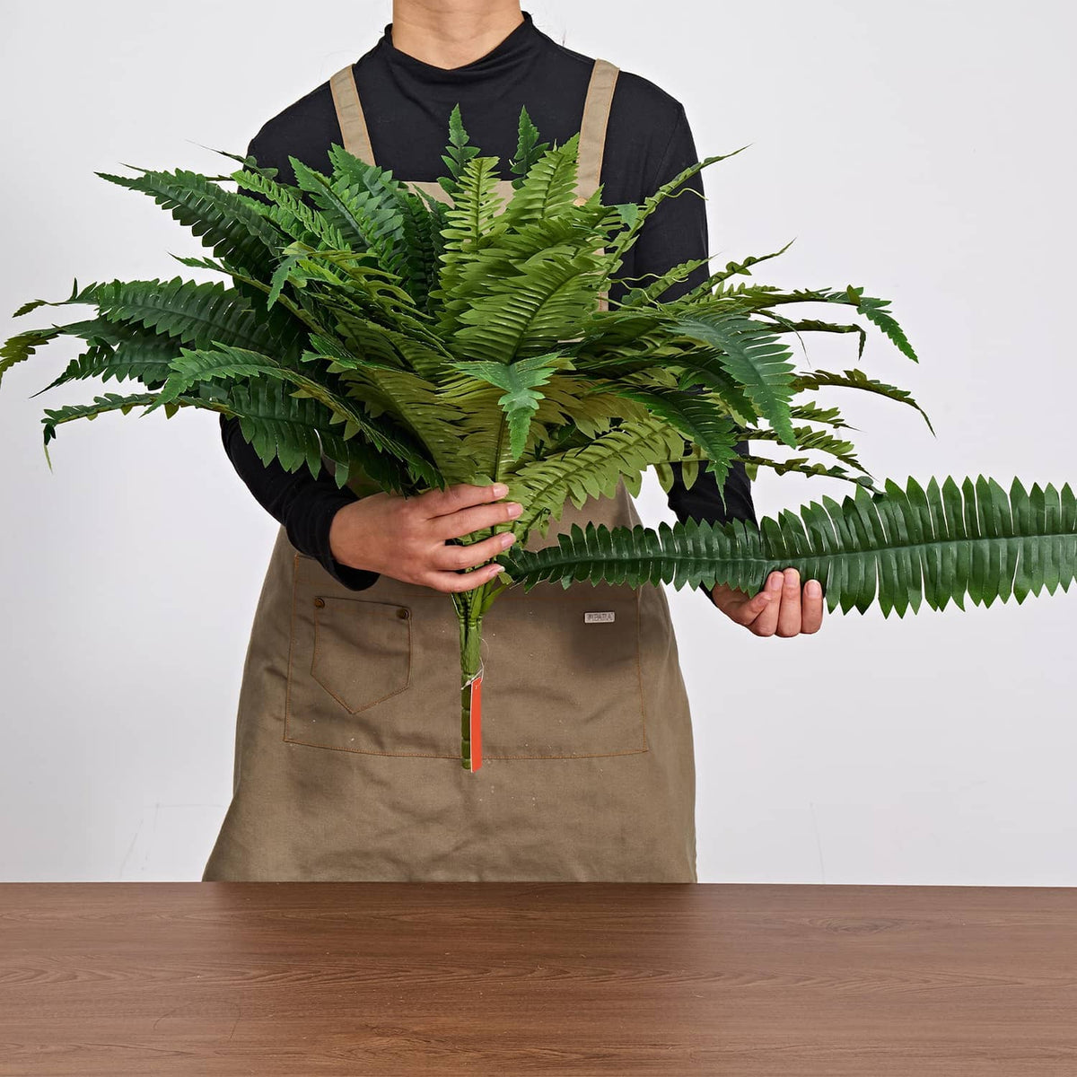 Artificial green fern plant held with full frond spread, flexible artificial leaves