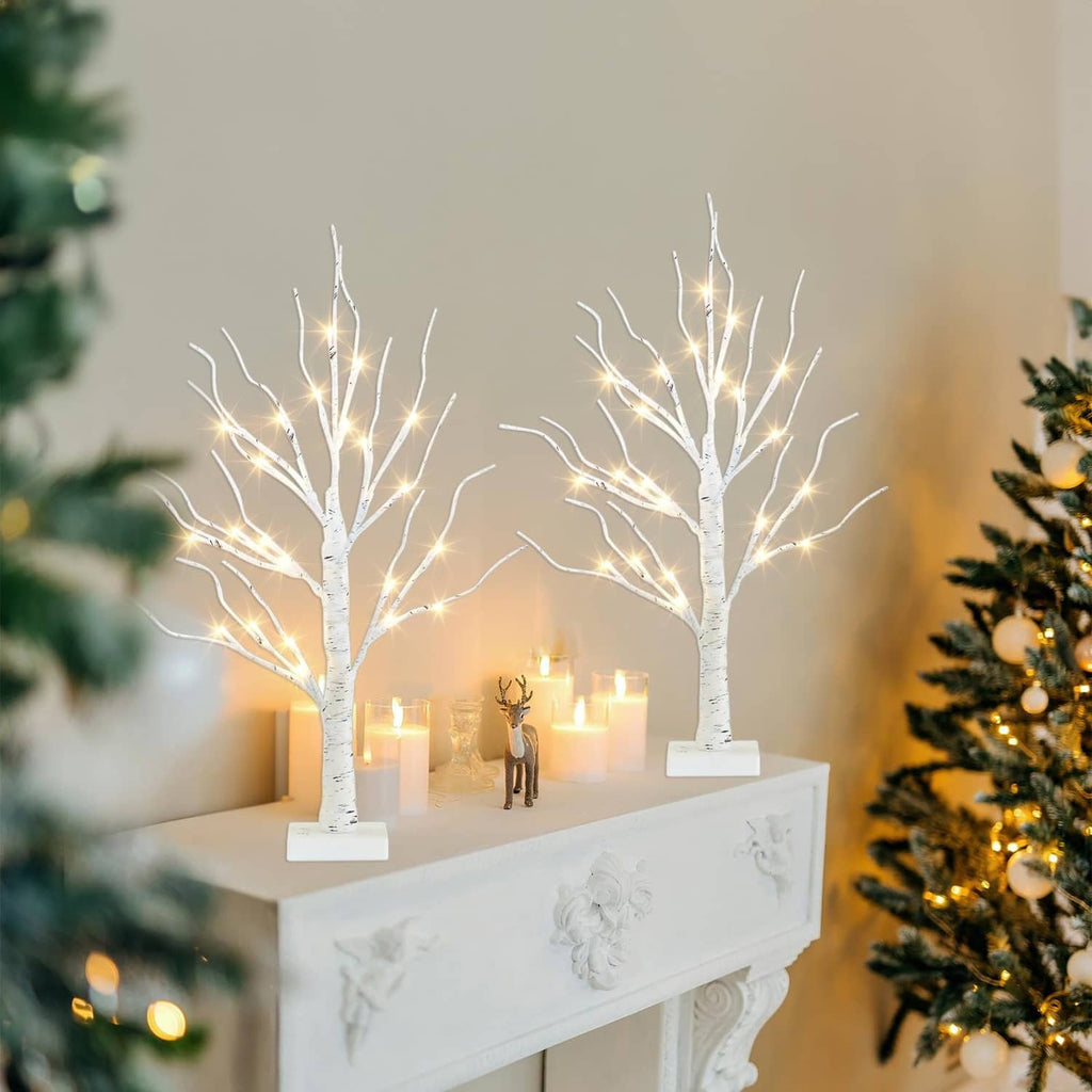 Two white LED birch tree decorations with warm lights on square bases atop a mantel