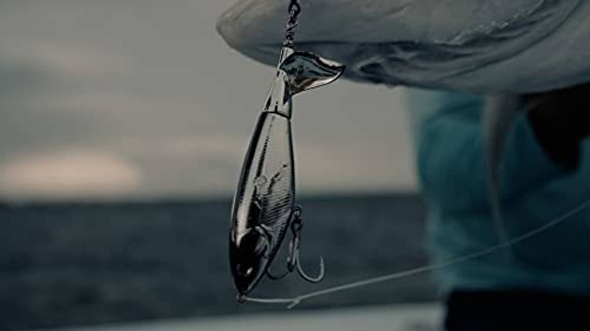 Topwater fishing lure suspended above water with treble hook