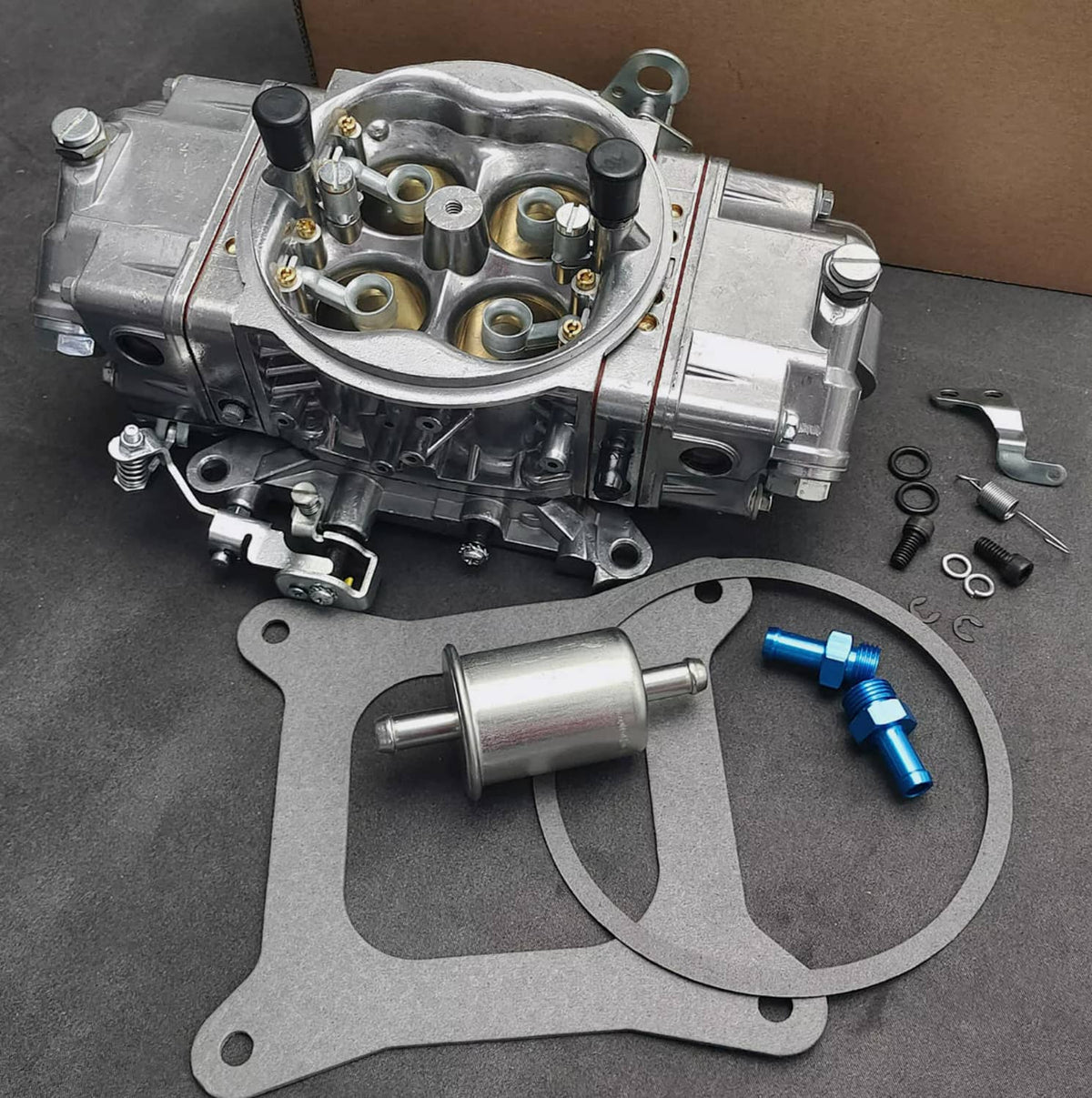Silver race carburetor assembly with gasket and seal parts, showing internal bores