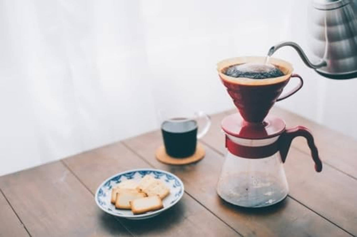 Red pour-over coffee brewer with carafe, ready to pour