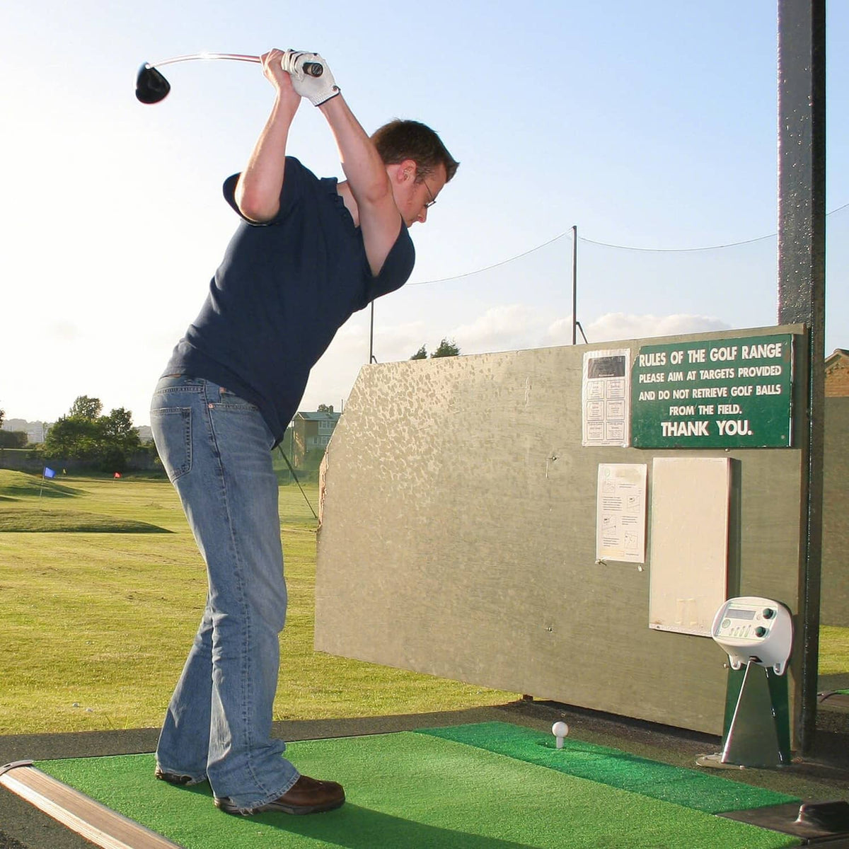 White rubber golf tee on a driving-range hitting mat beside a golfer