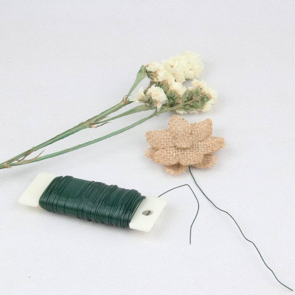 Green floral wire on cardboard spool with loose wire and small artificial flower heads