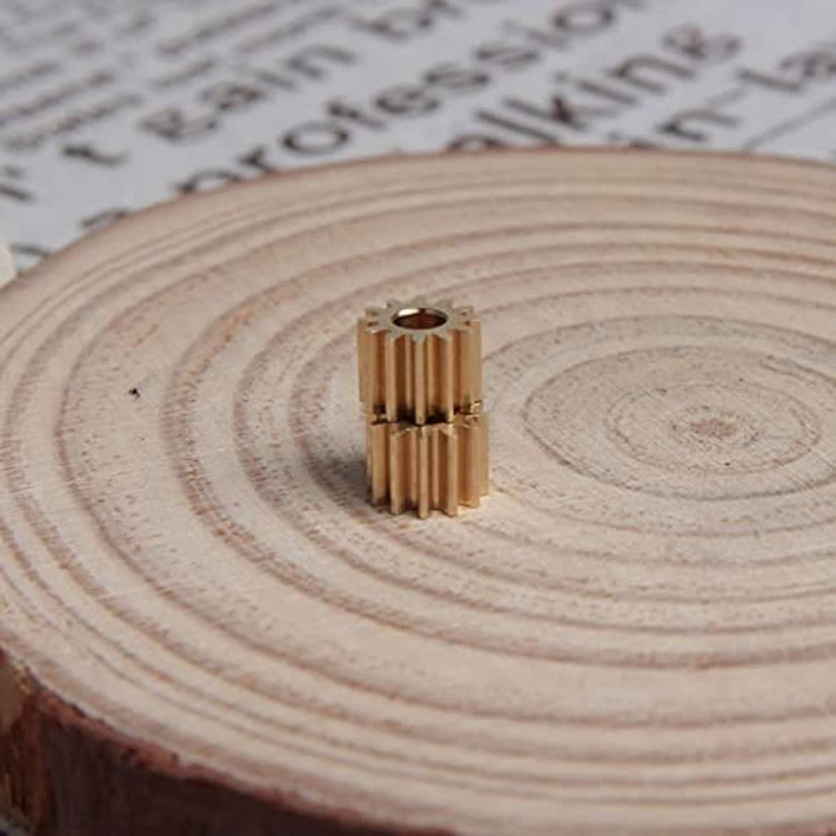 Copper 12-tooth spur gear with 3 mm bore, front view on a wooden slice