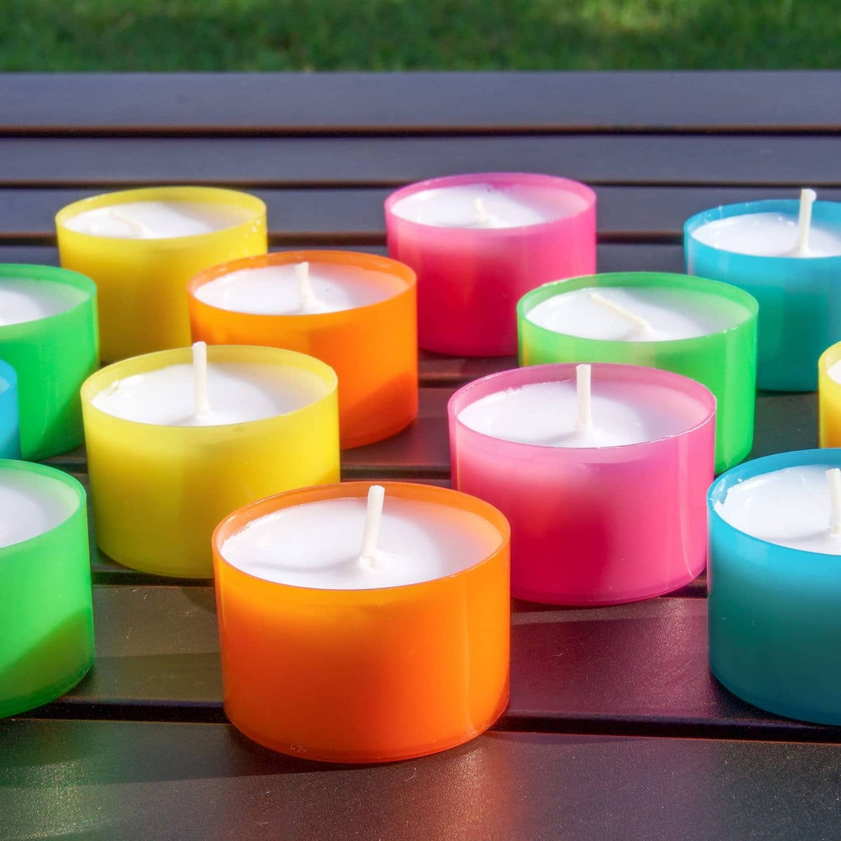Color tea light candles with lit wicks arranged together on a dark surface.