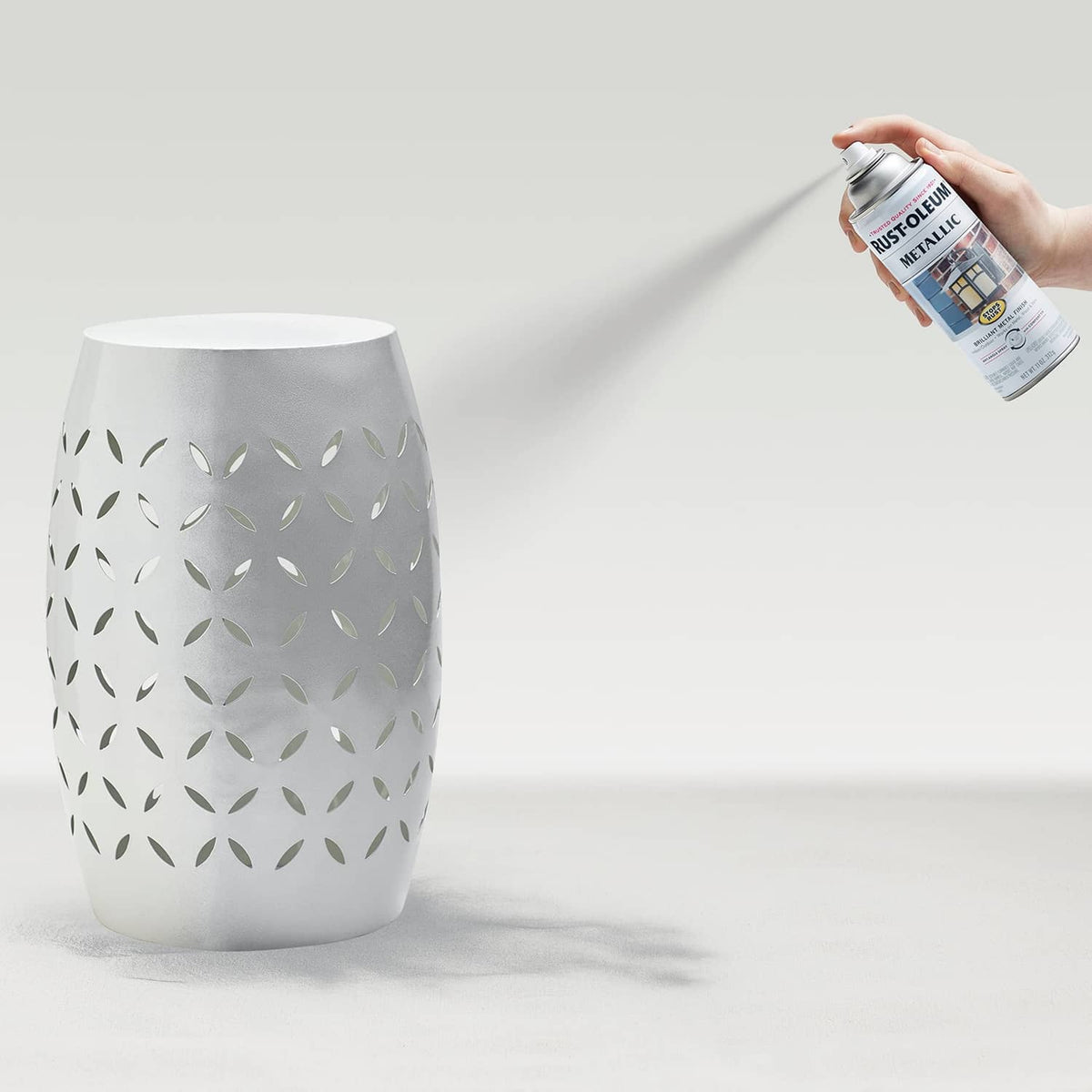 Hand holding silver Rust-Oleum spray can spraying patterned vase