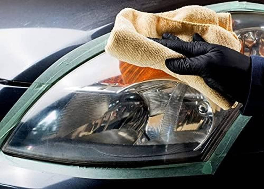 Car headlight lens being polished with a tan cloth by a gloved hand