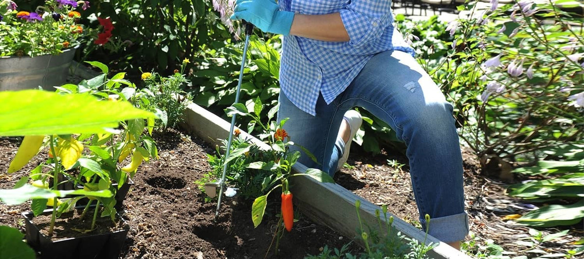 Drill tiller tool working in a raised garden bed, metal tines visible in soil
