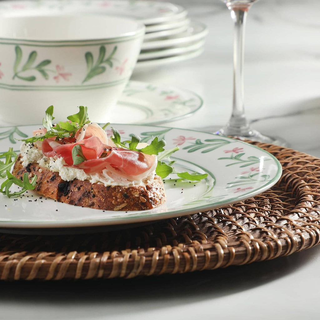 Floral serving plate with cured meat topping and greens, on white and green patterned dishes