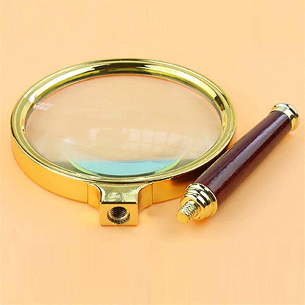 Magnifying glass close-up with gold lens housing, red handle, and small side screw