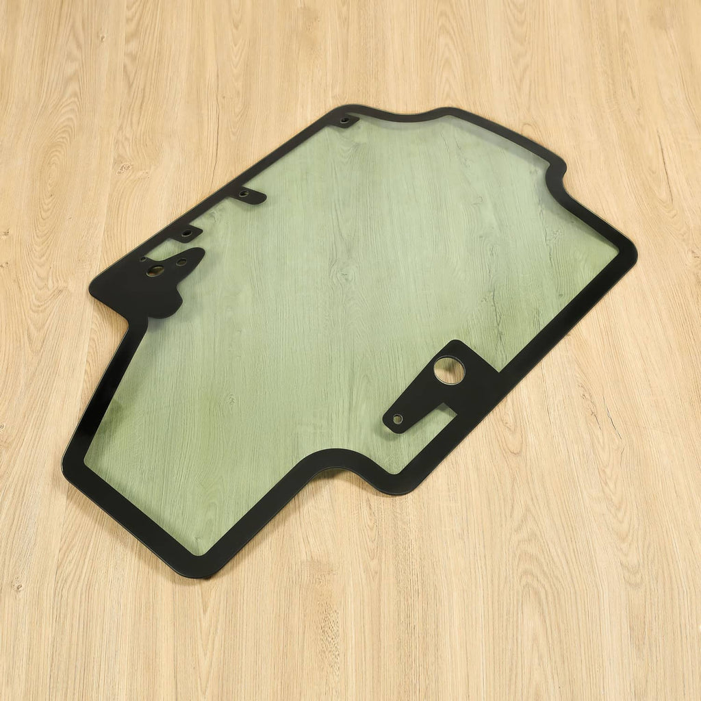 Skid steer door glass panel with black frame and latch/hinge hardware, tinted light green