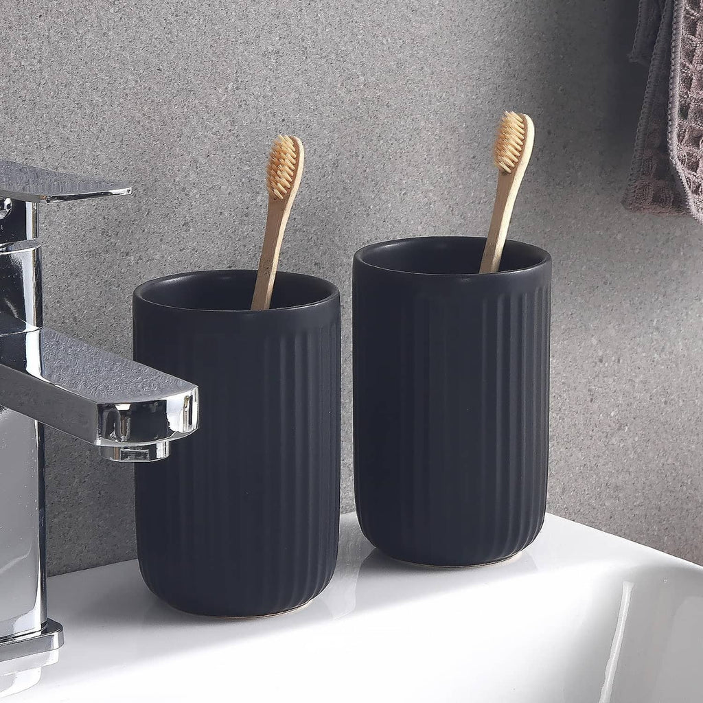 Two matte black ceramic toothbrush holders with ribbed sides beside bathroom faucet