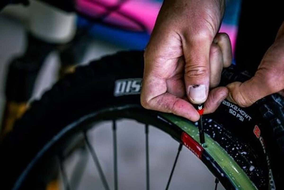 Hands installing a black tubeless valve stem into a wheel rim opening