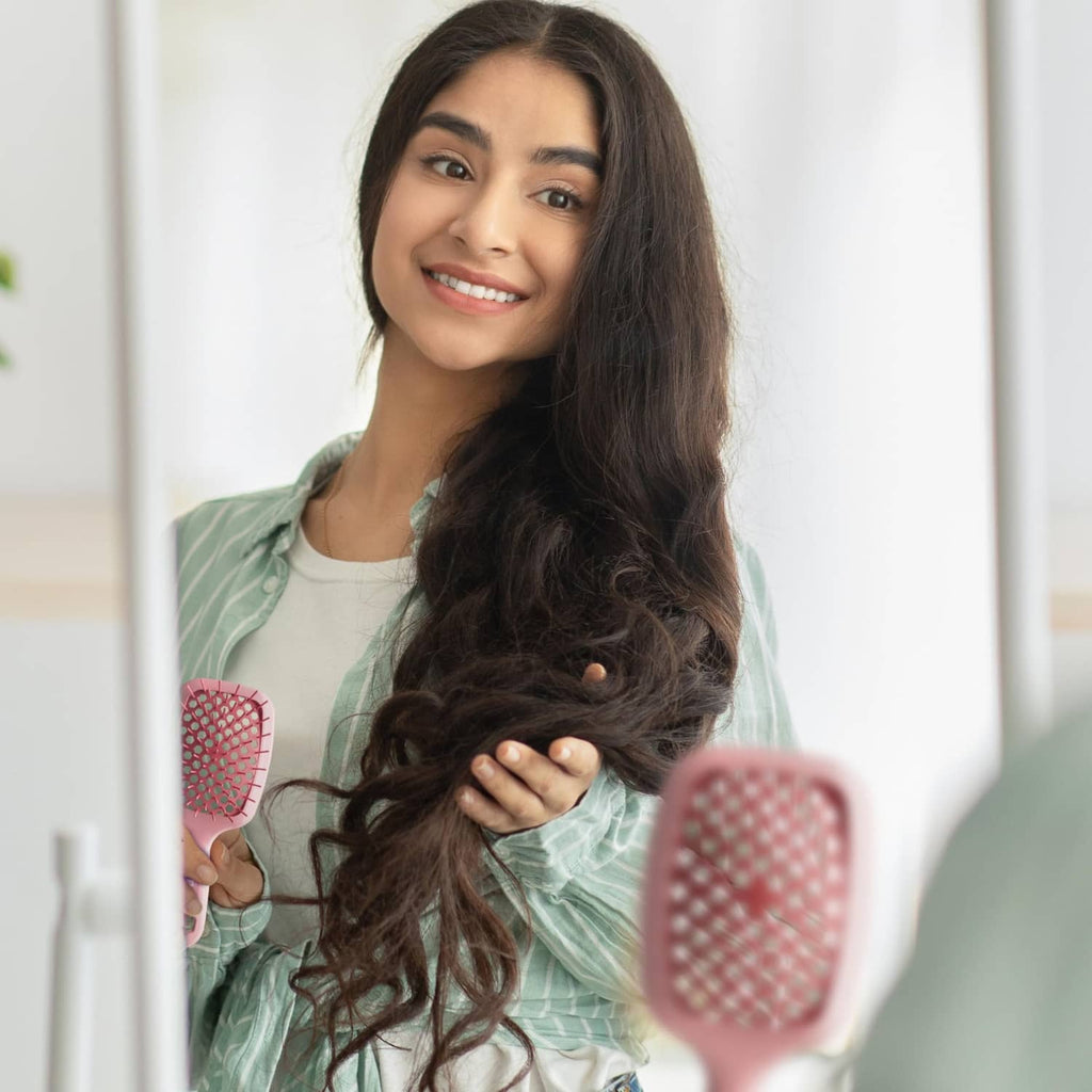 Light pink detangling hair brush with pink bristles held near dark hair