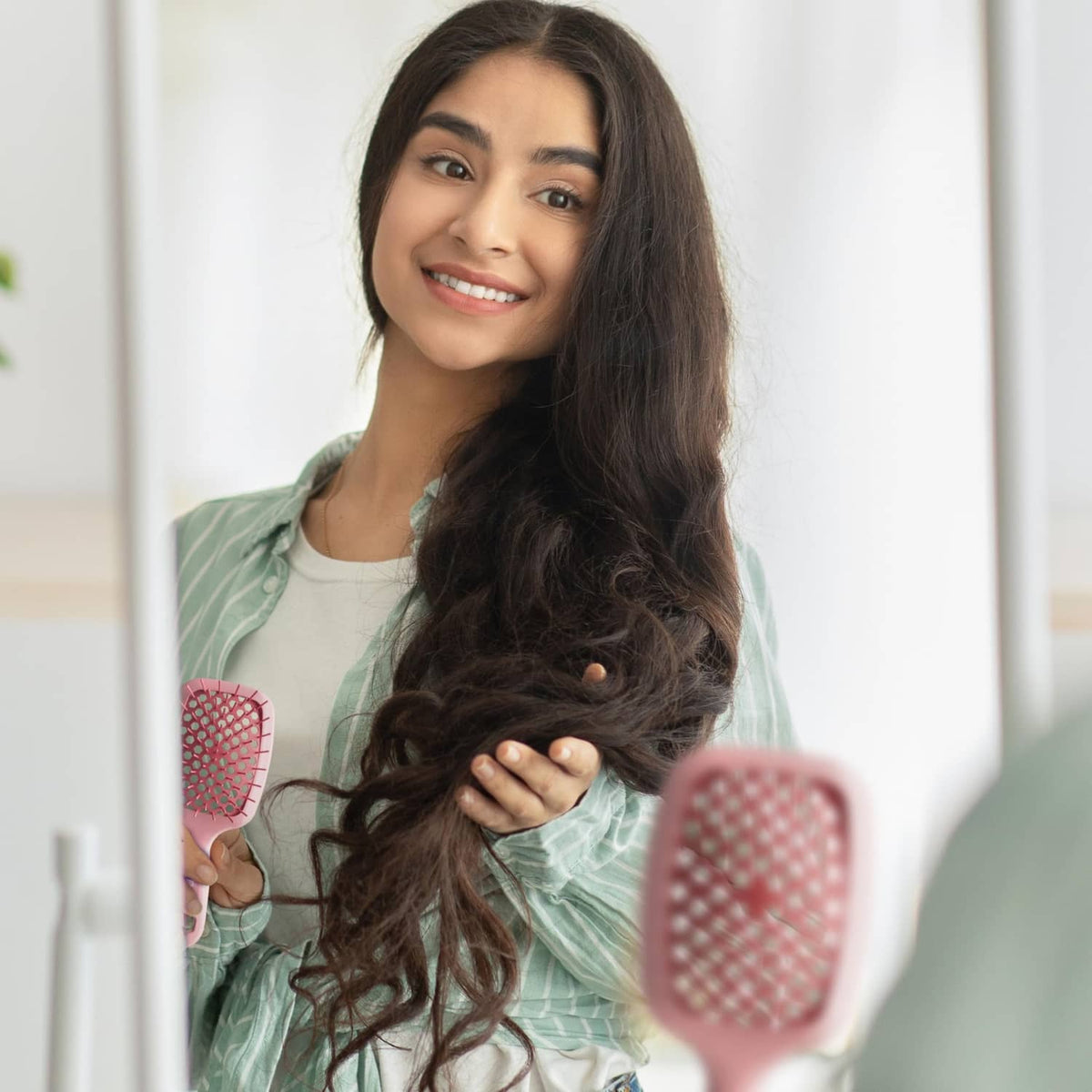 Light pink detangling hair brush with pink bristles held near dark hair