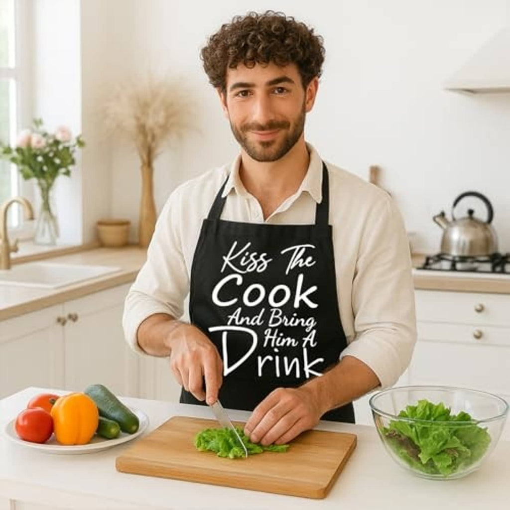 Black “Kiss The Cook” cooking apron worn over a light shirt with front pocket