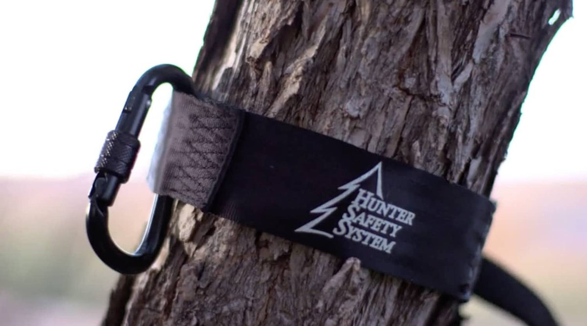 Dark green tree strap with Hunter Safety System logo and metal carabiner on bark