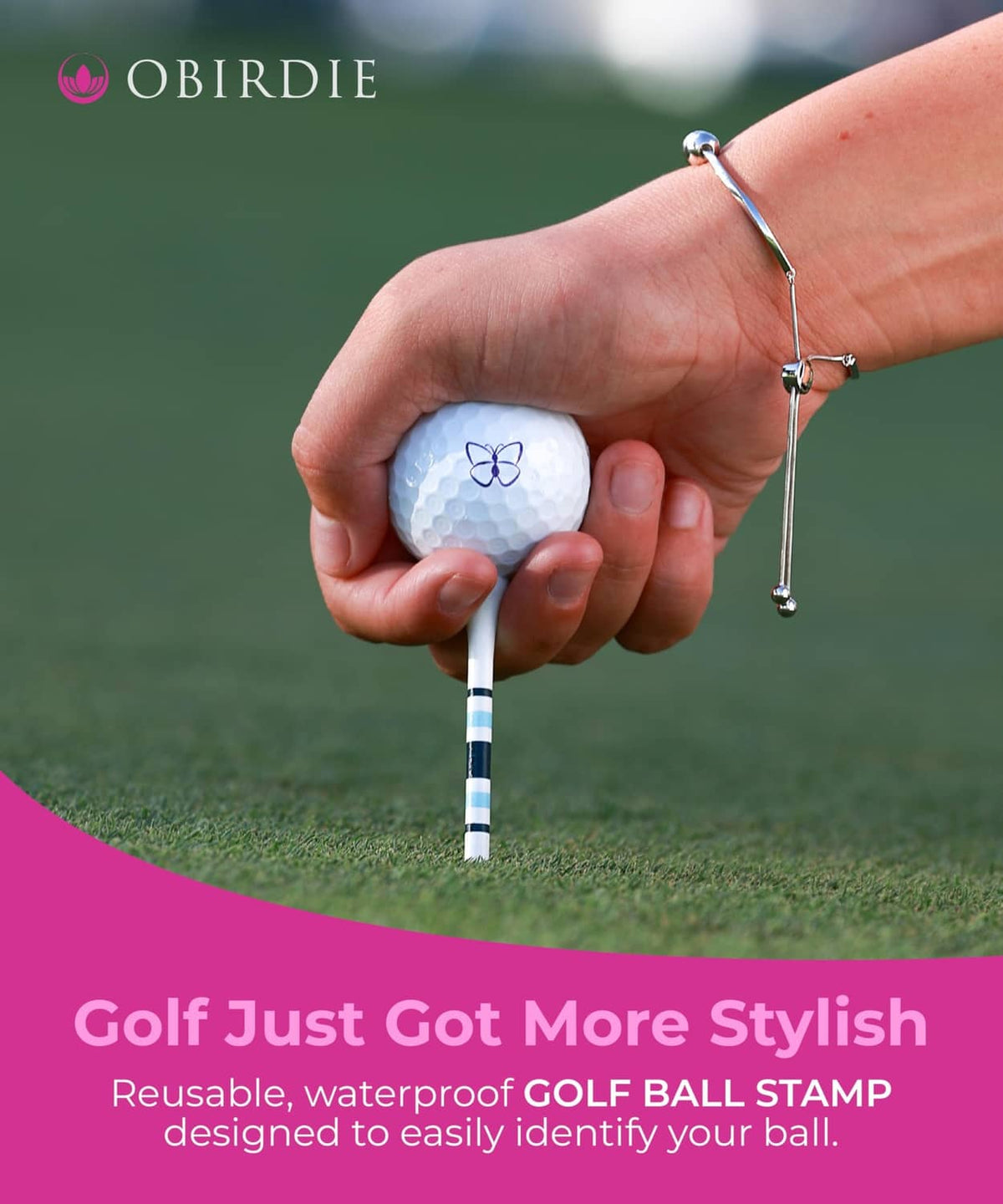 Hand holding a golf ball stamped with a blue butterfly icon on a green course