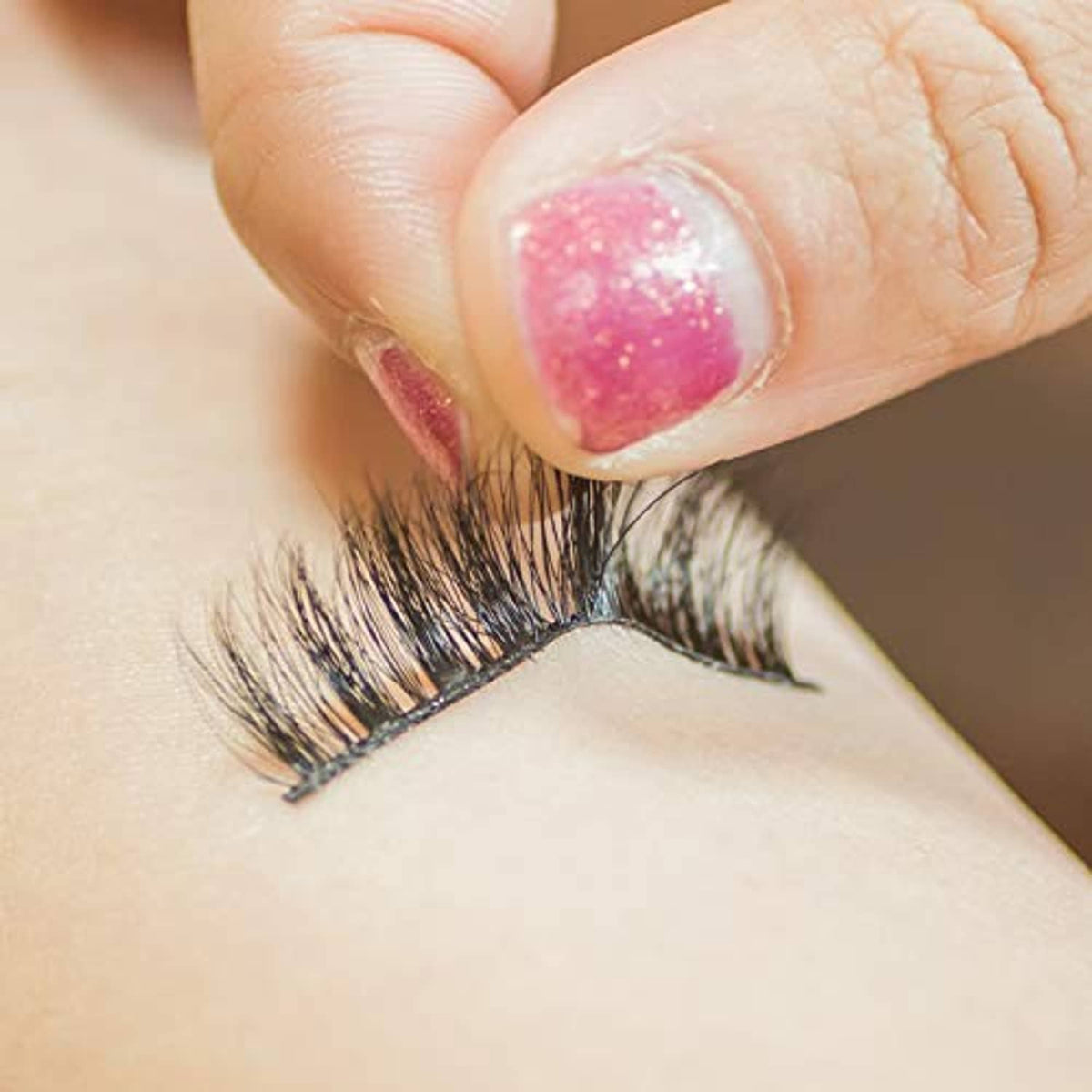 Close-up: false eyelash band with glue applied, lash tips aligned for placement.