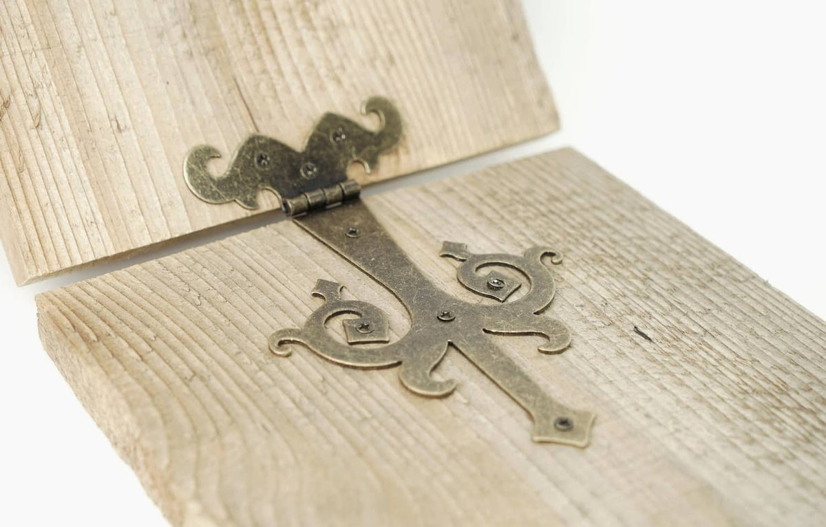 Bronze decorative strap hinge with ornate scroll design on wood boards