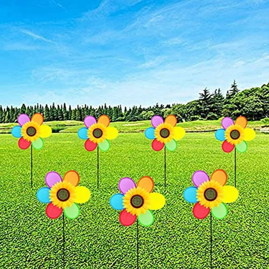 Multiple colorful sunflower pinwheel windmills on black stakes in a green yard