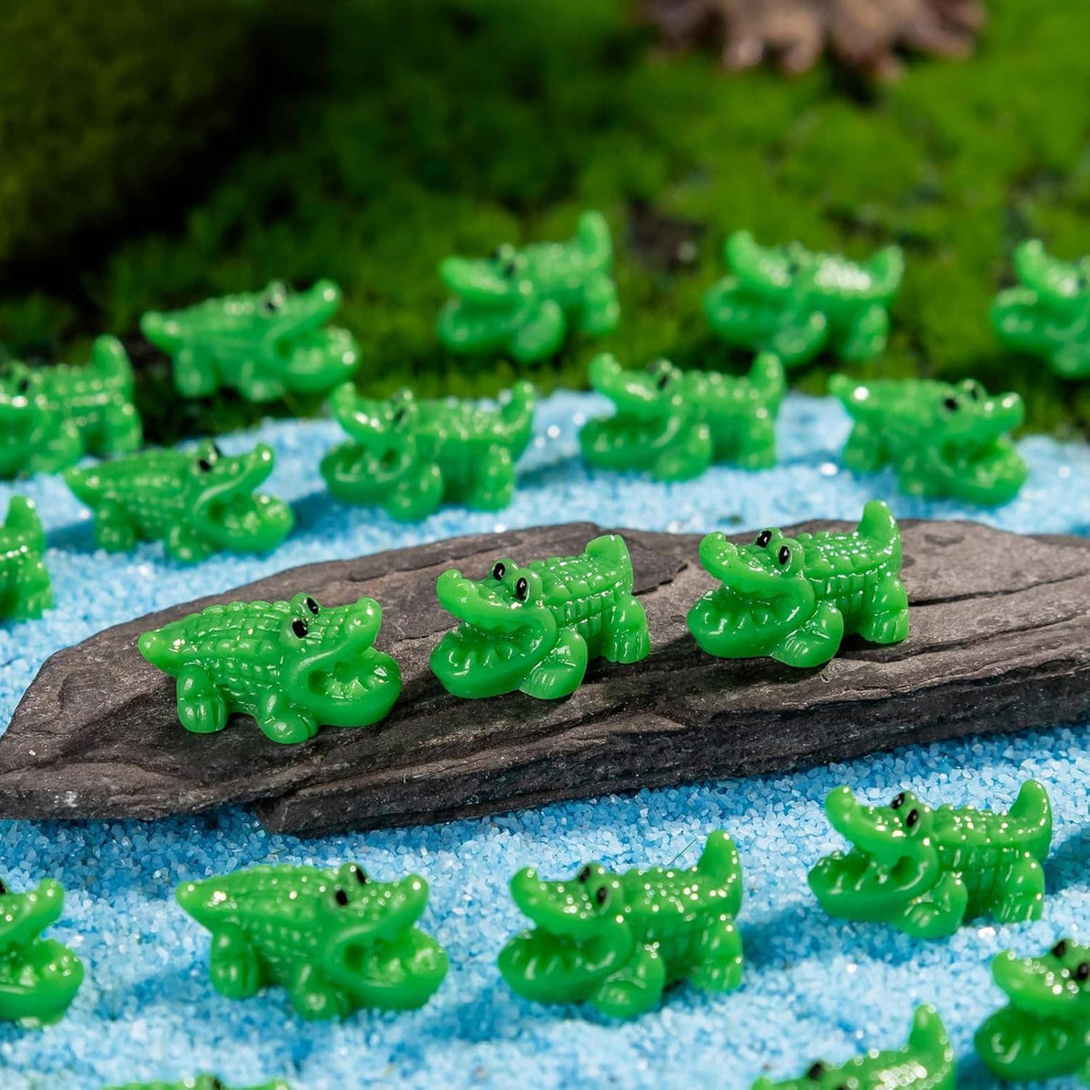Close-up of green mini crocodile resin figurines resting on a dark rock