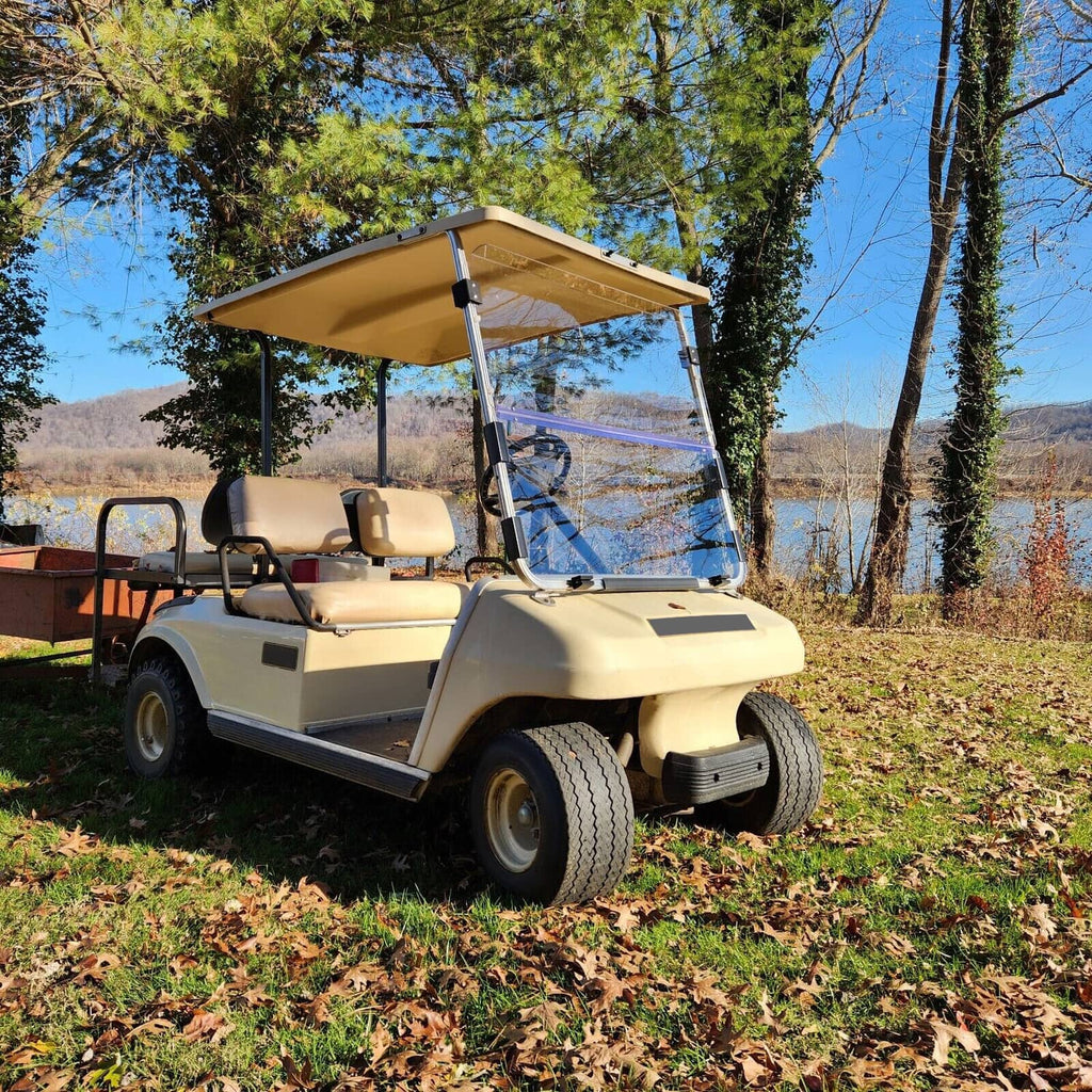 Clear folding golf cart windshield with black frame outdoors on a beige cart