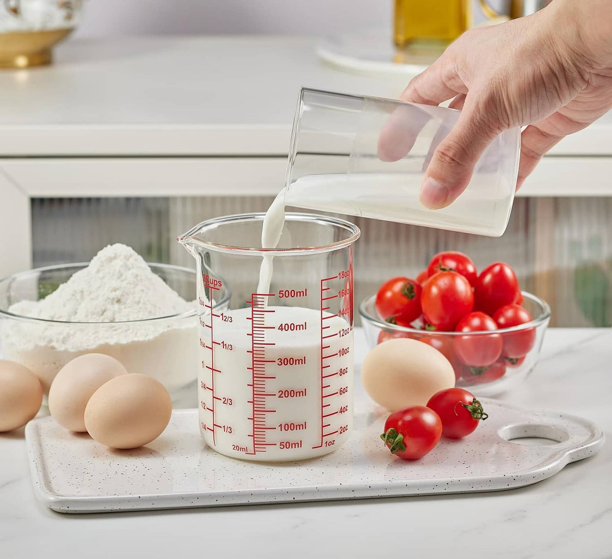 Clear glass measuring cup with red markings and V-shaped spout, pouring liquid