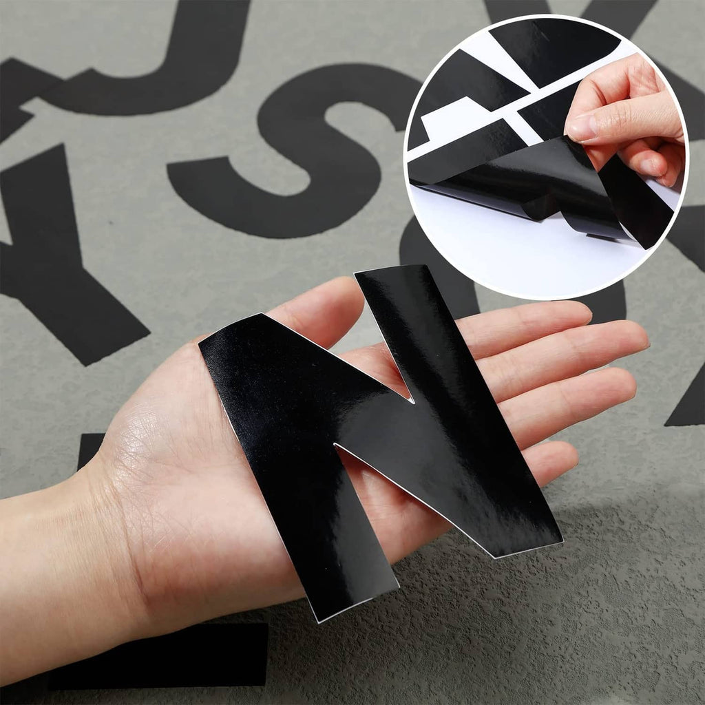 Hand applying bold black 4-inch vinyl letter stickers to a flat surface