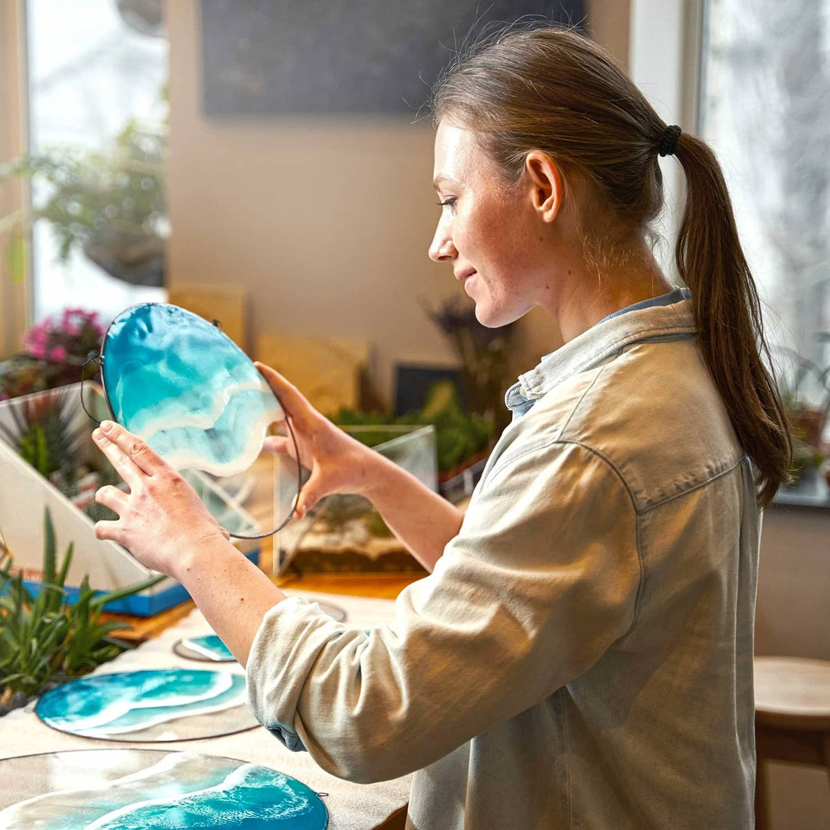 Person applying blue epoxy resin coating to a wooden tabletop for craft projects.