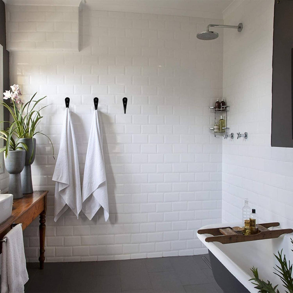 Black wall coat hooks holding folded towels above a bathroom countertop