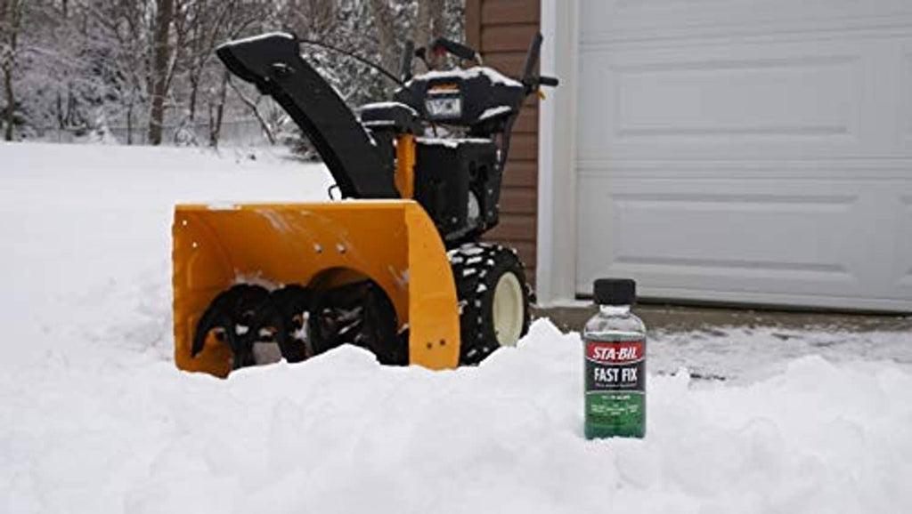Sta-Bil Fast Fix small engine treatment bottle standing in snow near snow blower