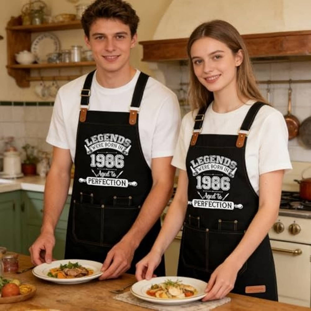 Matching black aprons with printed 1986 design, worn by a man and woman in kitchen.