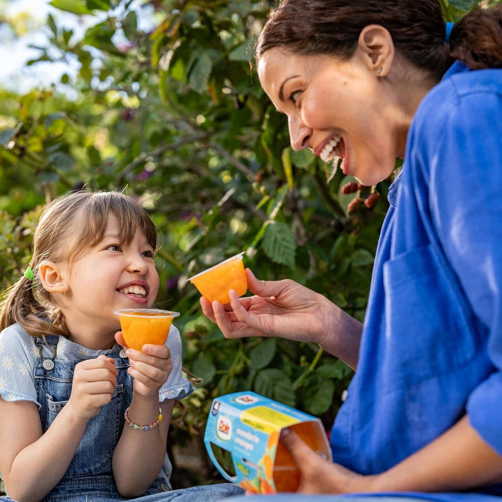 Child eating from a fruit bowl cup outdoors, with another cup held nearby