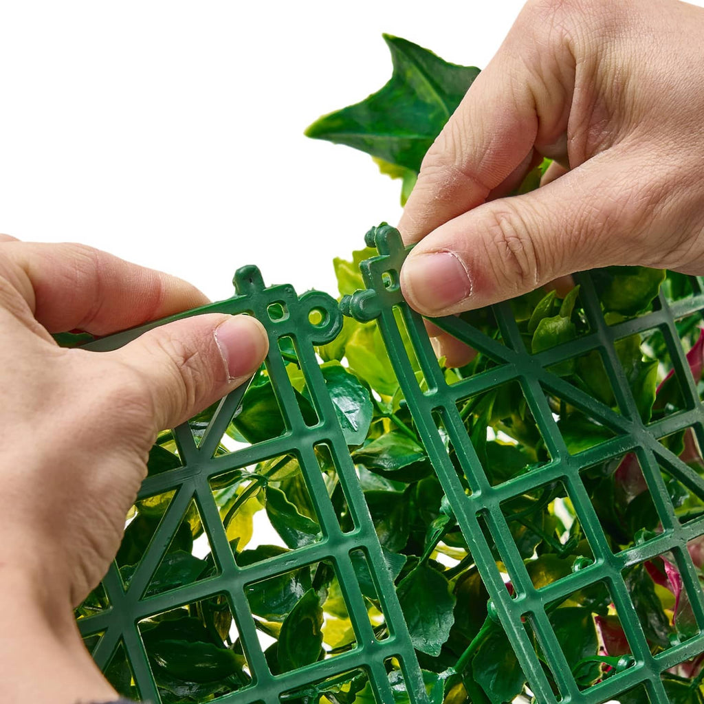 Artificial greenery panel with green plastic lattice backing, leaves held by hands
