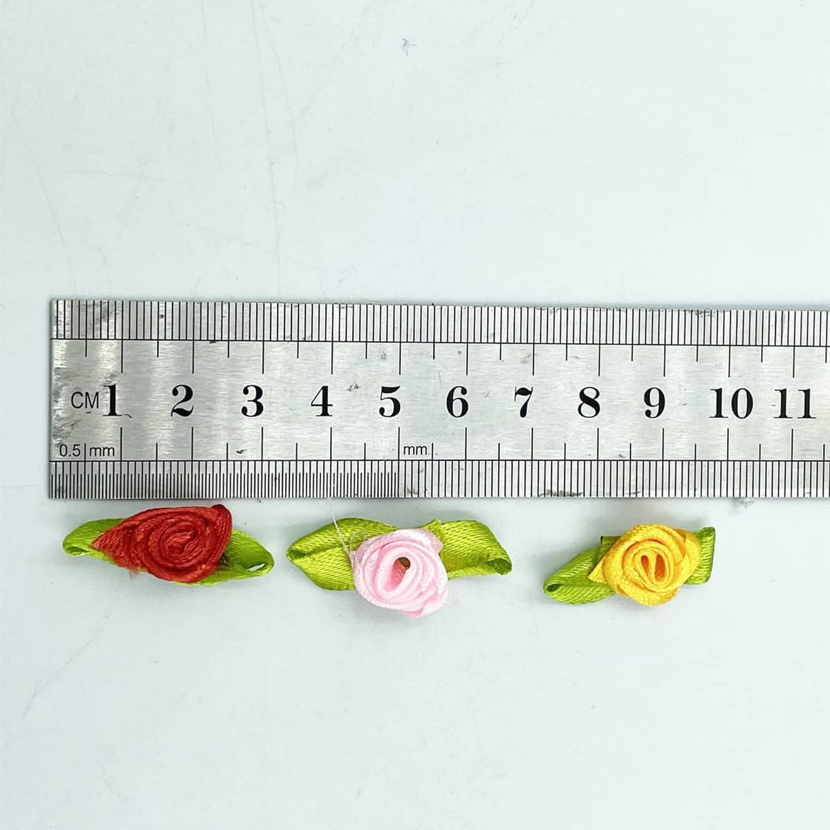 Mini ribbon rose flower with green leaves shown next to a ruler for size
