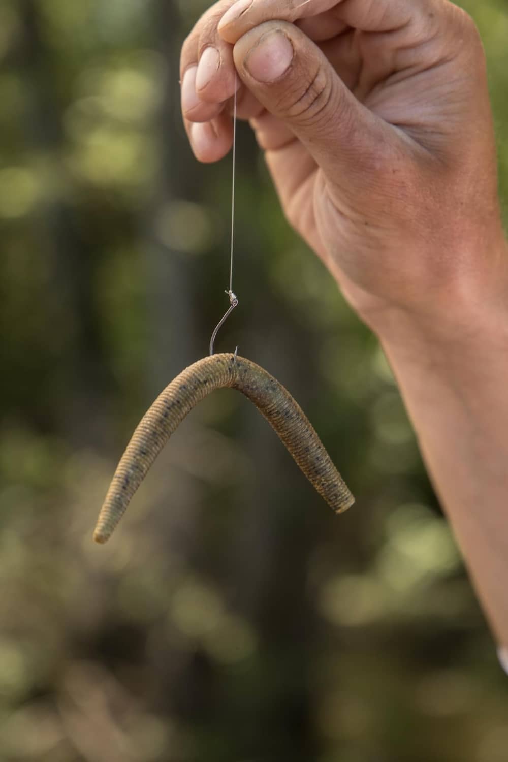 Green ribbed soft stick bait on fishing line, held in a hand